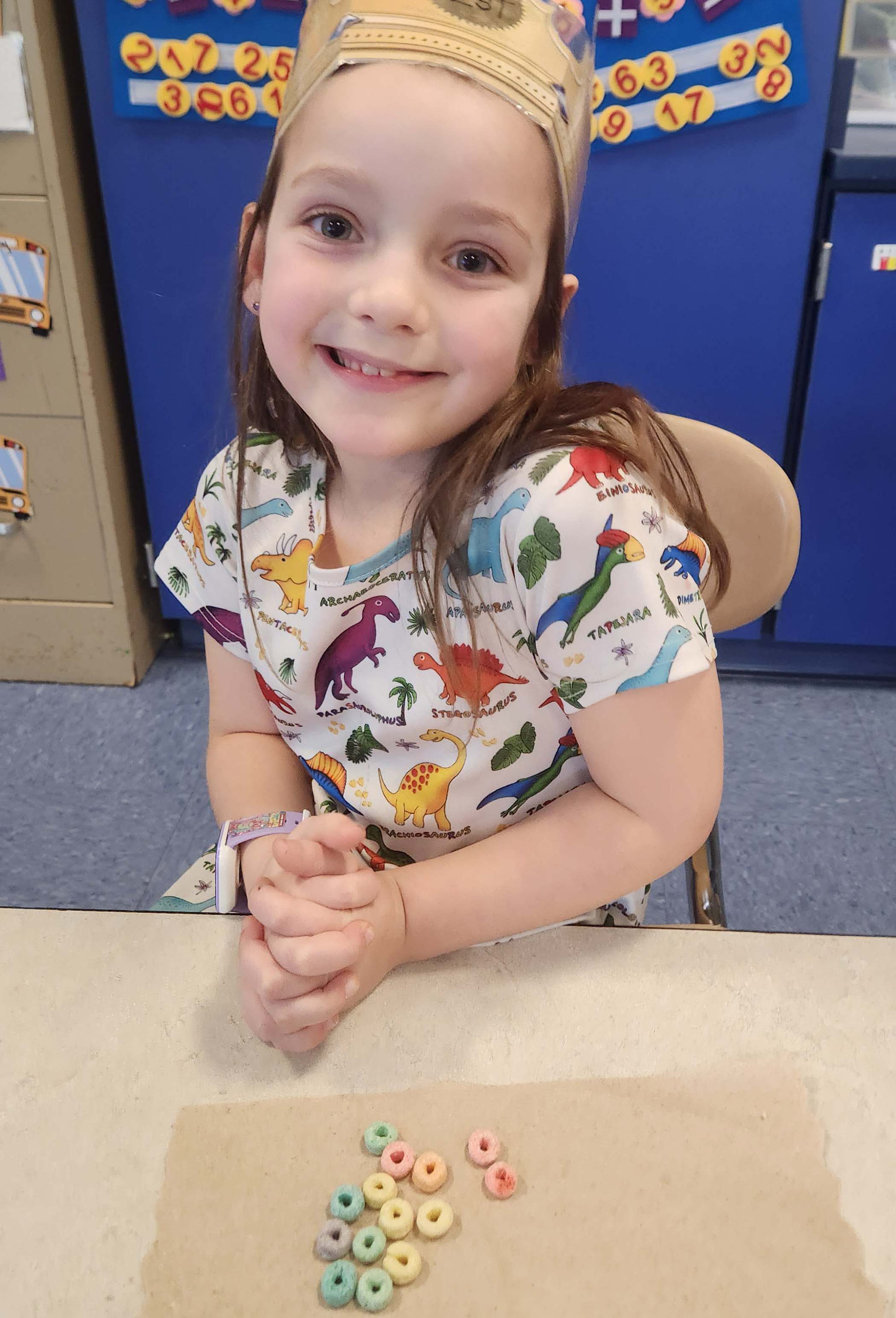 elementary student wearing a crown with fruit loops on desk