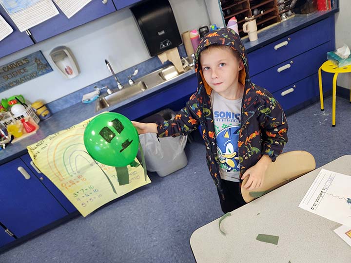 elementary student holding balloon with a face drawn on it